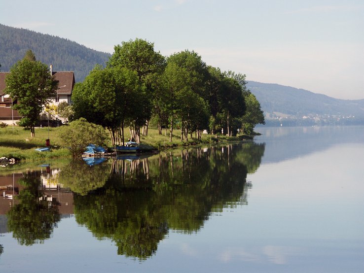 Rive du lac de Joux, avec petite maison, quelques arbres et quelques bateaux amarrés.