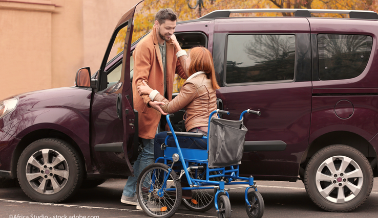 Un homme aide une femme en chaise roulante à entrer dans une voiture.