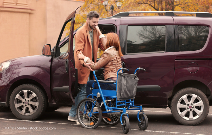 Un homme aide une femme en chaise roulante à entrer dans une voiture.