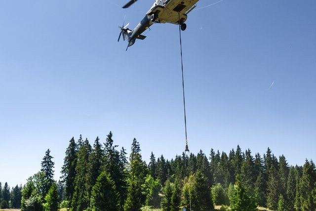 Un hélicoptère dépose une bâche remplie d'eau dans un réservoir, sur un alpage.