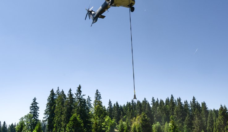 Un hélicoptère dépose une bâche remplie d'eau dans un réservoir, sur un alpage.