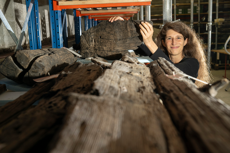 Image de Sophie Bärtschi, conservatrice aux Site et Musée romains d’Avenches et un fragment d'une ancienne barque gallo-romaine retrouvée sur le site d'un antique chantier naval. Photo | ARC Sieber