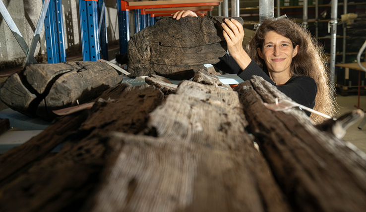 Image de Sophie Bärtschi, conservatrice aux Site et Musée romains d’Avenches et un fragment d'une ancienne barque gallo-romaine retrouvée sur le site d'un antique chantier naval. Photo | ARC Sieber