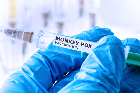Une main gantée tient une seringue et une dose de vaccin marquée "Monkey pox vaccination".