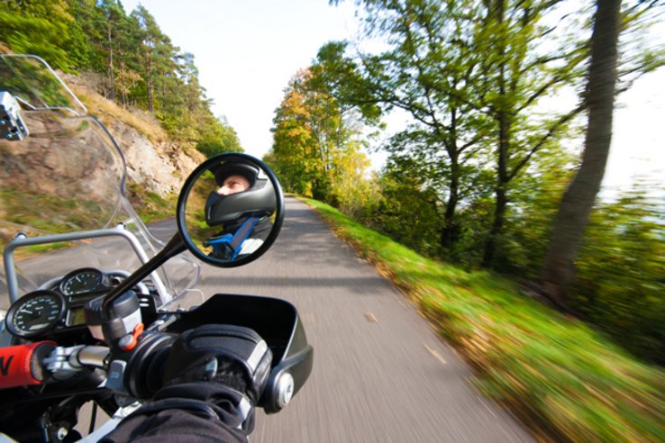 Motard vu dans le rétroviseur de sa moto roulant sur une route étroite.