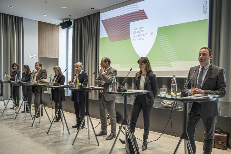 Les membres du Conseil d'Etat côte à côte debout derrière des tables hautes. Tout à leur gauche, le chancelier en train de parler.