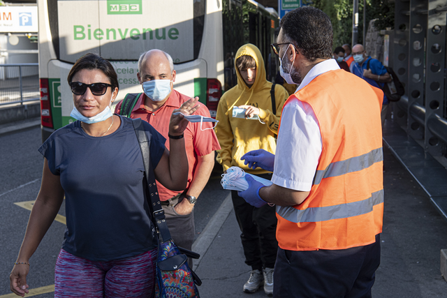 Un homme portant gants en latex et gilet fluorescent distribue des masques aux passants près de la gare de Morges.