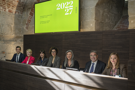 Les sept membres du gouvernement assis à leurs pupitres dans la salle des médias du château cantonal.