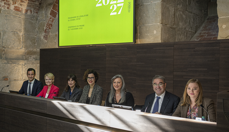 Les sept membres du gouvernement assis à leurs pupitres dans la salle des médias du château cantonal.