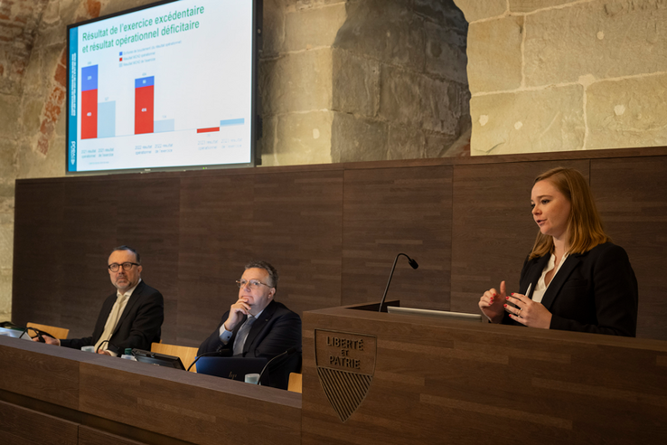 Les trois personnes derrière leur pupitre, en conférence de presse. Madame Dittli se tient debout.