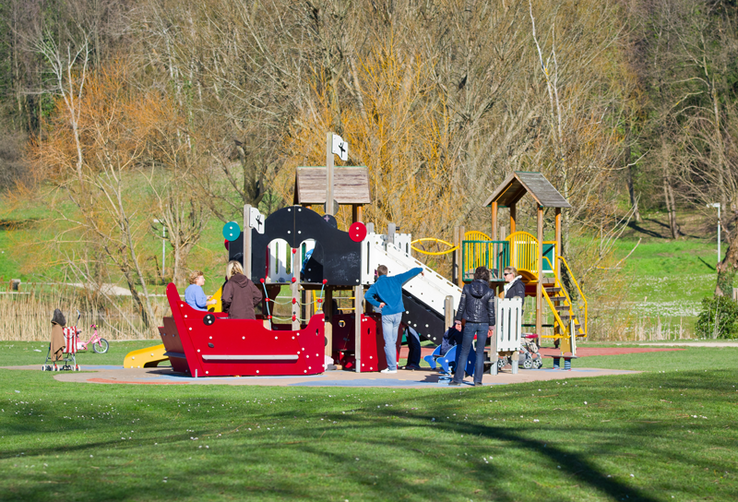Enfants jouant dans une installation dans un parc public, sous le regard de quelques parents.