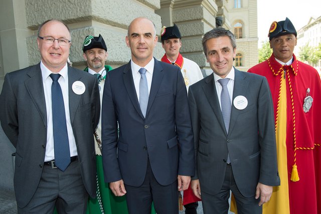 Les trois personnages posent sur la place fédérale. Derrière, des huissiers aux livrées des deux cantons.