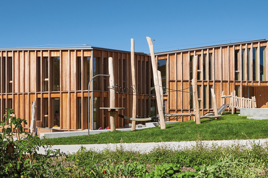 Un bâtiment allongé d'un étage sur rez, constitué de lames de bois verticales.