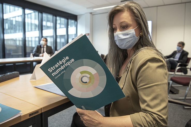 Madame Gorrite, masquée, tient la brochure "Stratégie numérique du Conseil d'Etat"