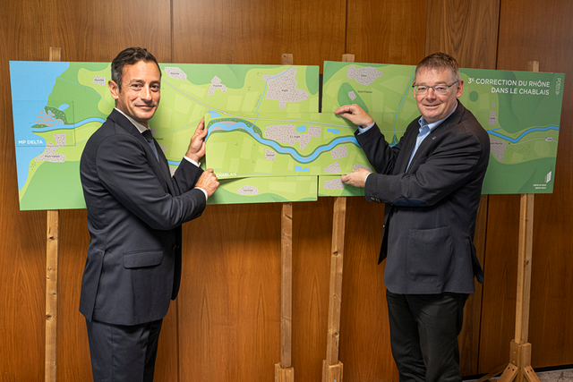 les deux personnages, debout devant une carte du projet, se serrent la main.
