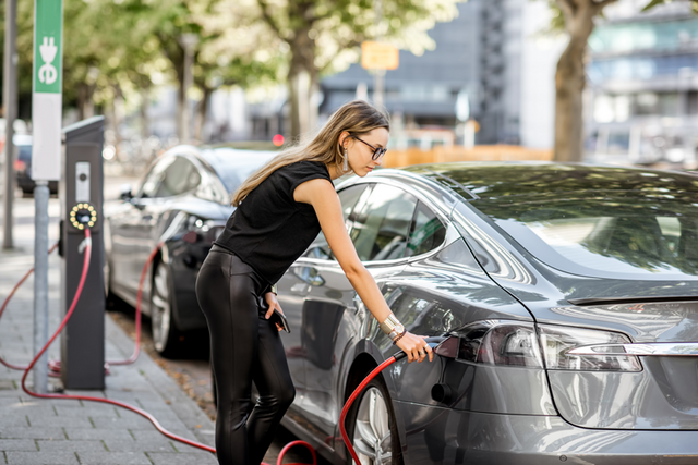 Une femme a branché un véhicule électrique à une borne de recharge.