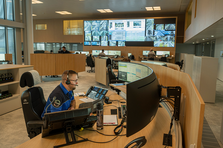Un opérateur à son poste de travail dans la grande salle de la centrale d'alarme. Au fond, un mur d'écrans avec des informations et images du trafic routier.