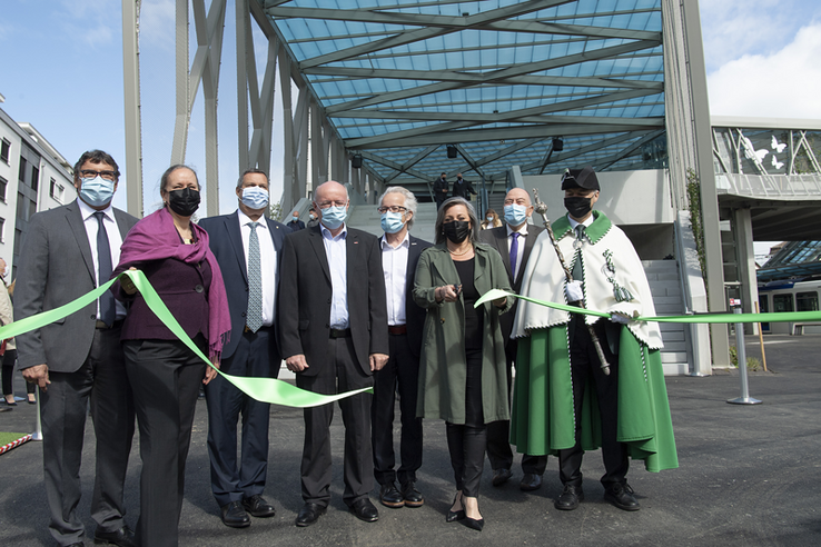 Les personnages posent en groupe au pied de la passerelle, derrière le ruban qui vient d'être coupé par la présidente du Conseil d'Etat, ciseaux en mains.