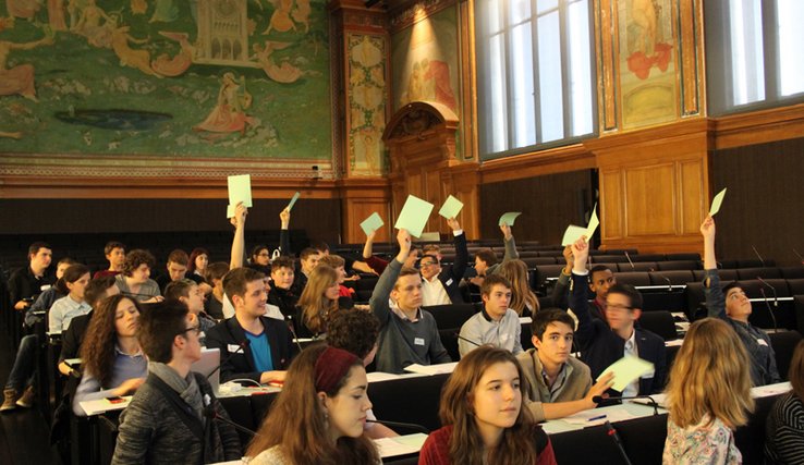 les jeunes siègent dans l'aula du Palais de Rumine, durant un vote. Des mains sont levées, tenant des bulletins.