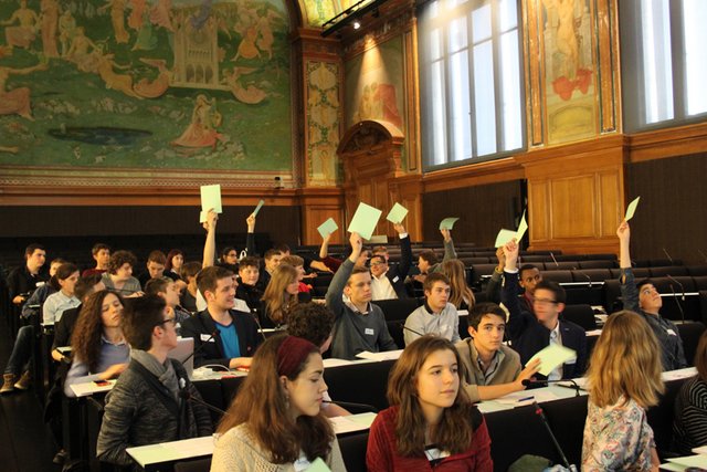 les jeunes siègent dans l'aula du Palais de Rumine, durant un vote. Des mains sont levées, tenant des bulletins.