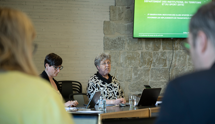 La présidente, assise à une table, durant la conférence de presse. Au mur, un écran affiche une slide du support de présentation.