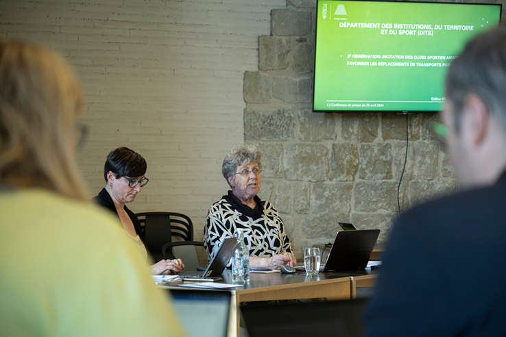 La présidente, assise à une table, durant la conférence de presse. Au mur, un écran affiche une slide du support de présentation.