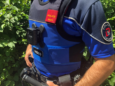 Un agent (on ne voit que son tronc) porteur d'une caméra-piéton, collée à son buste au niveau du plexus.