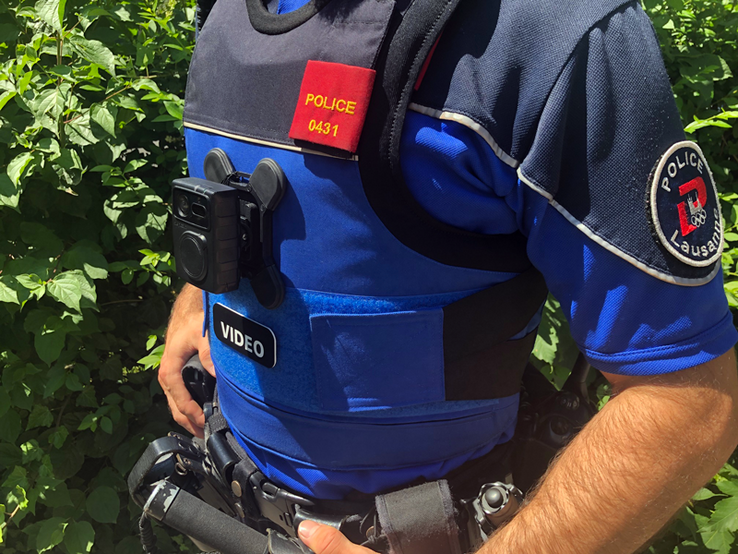 Un agent (on ne voit que son tronc) porteur d'une caméra-piéton, collée à son buste au niveau du plexus.