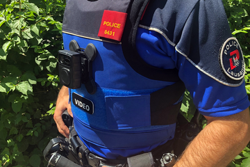 Un agent (on ne voit que son tronc) porteur d'une caméra-piéton, collée à son buste au niveau du plexus.