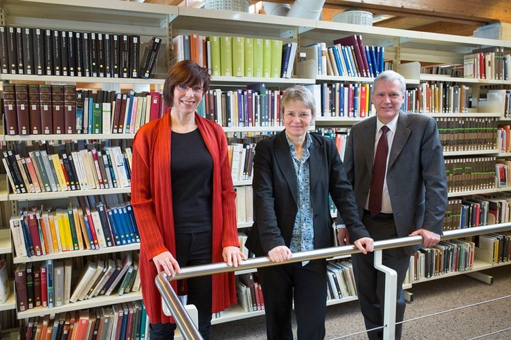 Les trois personnages posent dans la Bibliothèque, appuyés à la rambarde d'un escalier. Derrière, des rayonnages de livres.