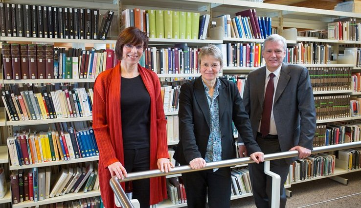 Les trois personnages posent dans la Bibliothèque, appuyés à la rambarde d'un escalier. Derrière, des rayonnages de livres.