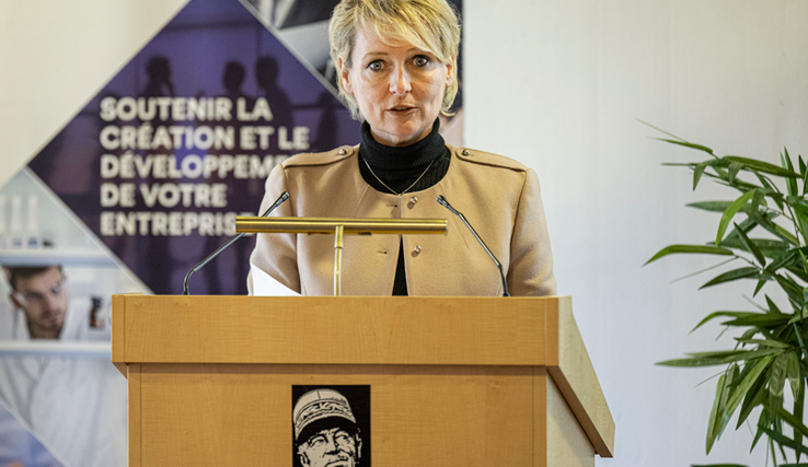 La conseillère d'Etat parle en conférence de presse, derrière un pupitre où s'affiche le visage du Général-Guisan (on est à Verte-Rive, à Pully). Derrière, une affiche sur laquelle on lit "Soutenir la création et le développement de votre entreprise".