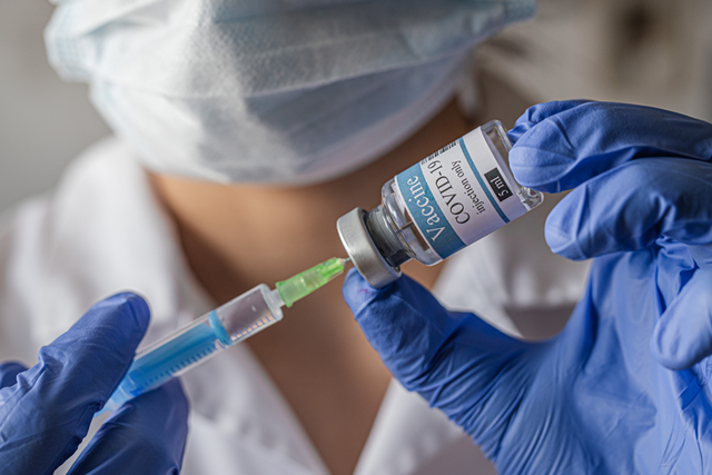 Quelqu'un portant des gants en vinyle remplit une seringue de vaccin.