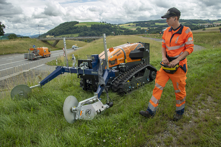 Une cantonnière conduit une machine de fauchage au bord d'une route.