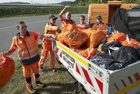 Des travailleurs jettent des sacs de déchets sur le plateau d'une camionnette au bord d'une route.