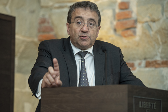 Le conseiller d'Etat en conférence de presse, il lève l'index droit en parlant.