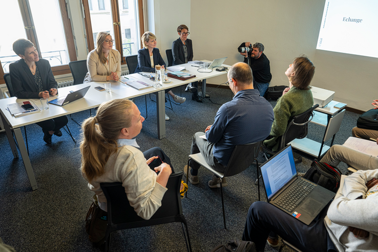 Scène de conférence de presse. Les quatre personnes assises face à des journalistes. Au fond, un photographe au travail.