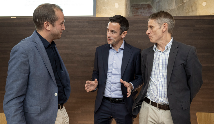 Les trois personnages discutent, debout, à l'issue de la conférence de presse.
