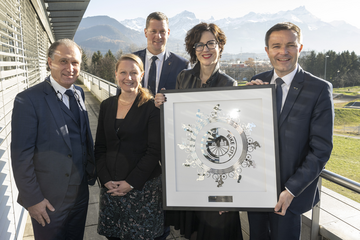 Les personnages posent sur un balcon du centre cycliste de l'UCI à Aigle, sur fond de montagnes ensoleillées.