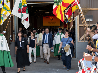 Patrick Simonin à la sortie d'une halle entouré de diverses personnalités politiques, sous une rangée de drapeaux.