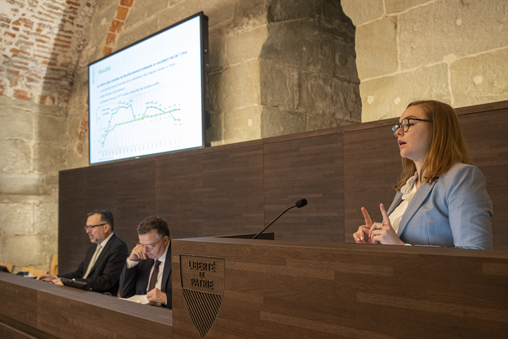 La conseillère d'Etat parle en conférence de presse, deux index pointés vers le haut.