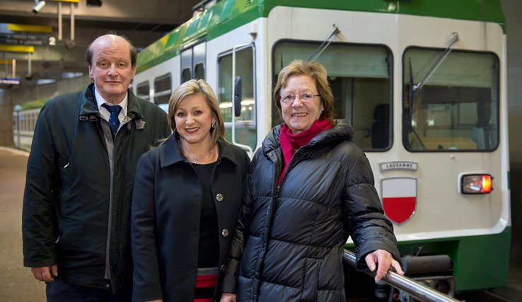 Les trois personnages posent à la station Flon devant une rame du LEB.