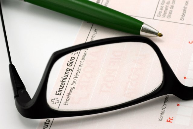 Illustration: une paire de lunettes posée sur un bulletin de versement.