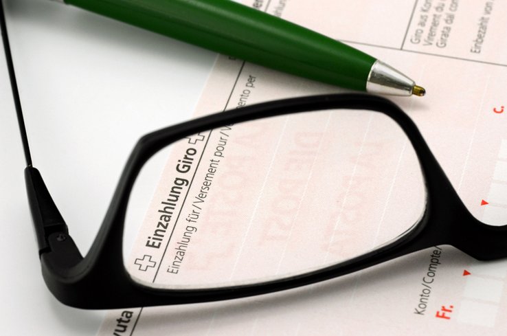 Illustration: une paire de lunettes posée sur un bulletin de versement.