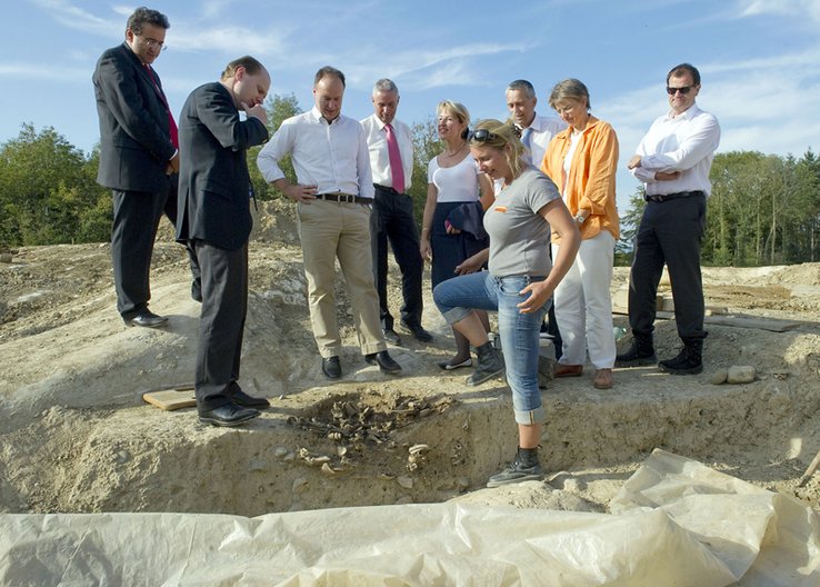 Le Conseil d'Etat près d'une tombe du Mormont, que leur présente Mme Brunetti, cheffe du chantier.