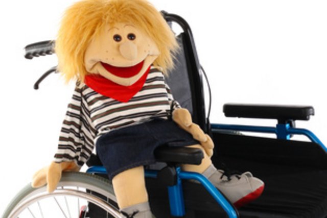 Une chaise roulante avec une marionnette rieuse assise dedans.