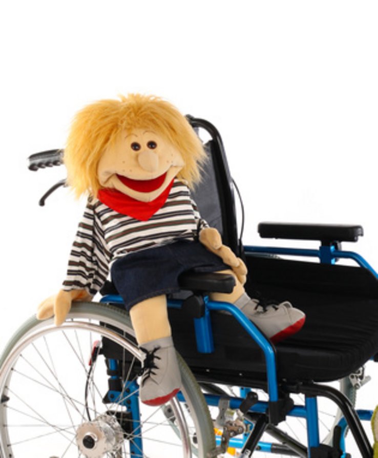 Une chaise roulante avec une marionnette rieuse assise dedans.