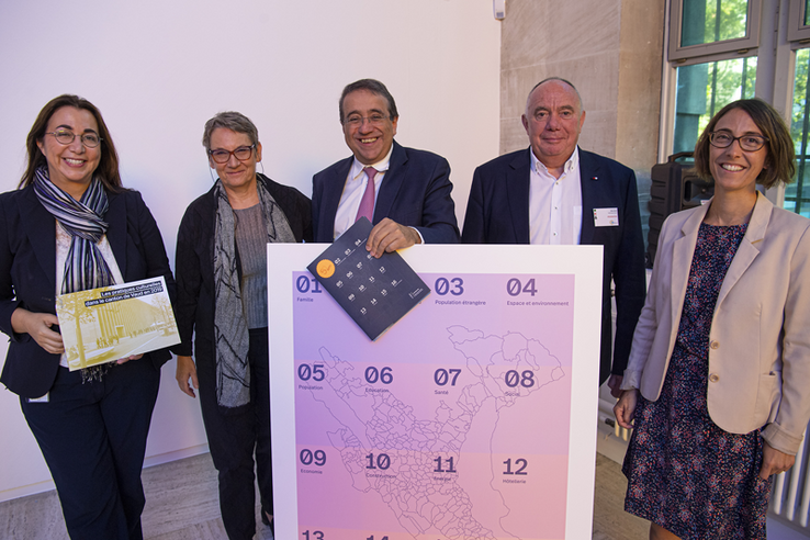 Les personnages posent derrière une carte montrant le découpage communal d'un district.