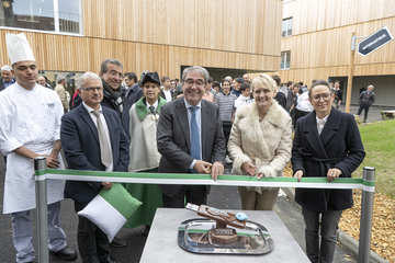 Les personnages tiennent les ciseaux, derrière le ruban. Sur une table au premier plan, une pièce en chocolat en forme de clé USB géante, confectionnée par les jeunes en formation au COFOP.