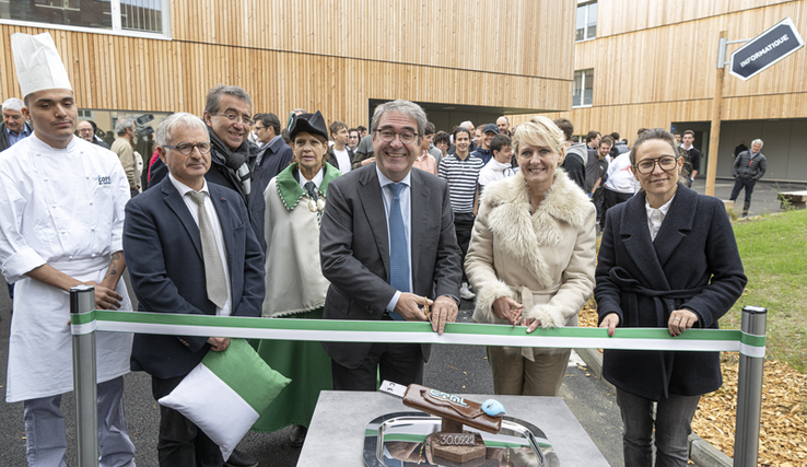 Les personnages tiennent les ciseaux, derrière le ruban. Sur une table au premier plan, une pièce en chocolat en forme de clé USB géante, confectionnée par les jeunes en formation au COFOP.